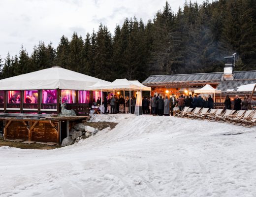 Vue large du chalet Le Clos Bernard illuminé sous la neige pour une réception de mariage.