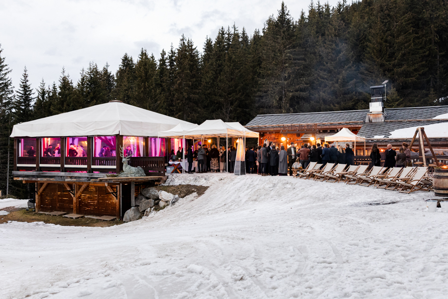 Vue large du chalet Le Clos Bernard illuminé sous la neige pour une réception de mariage.